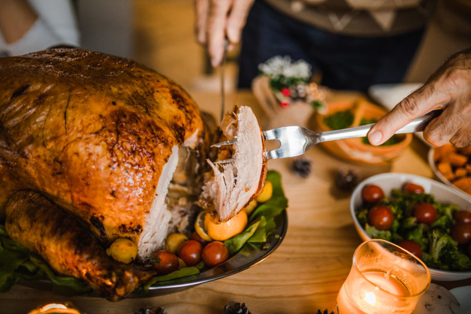 Close up of unrecognizable person carving white meat during dinner at dining table.