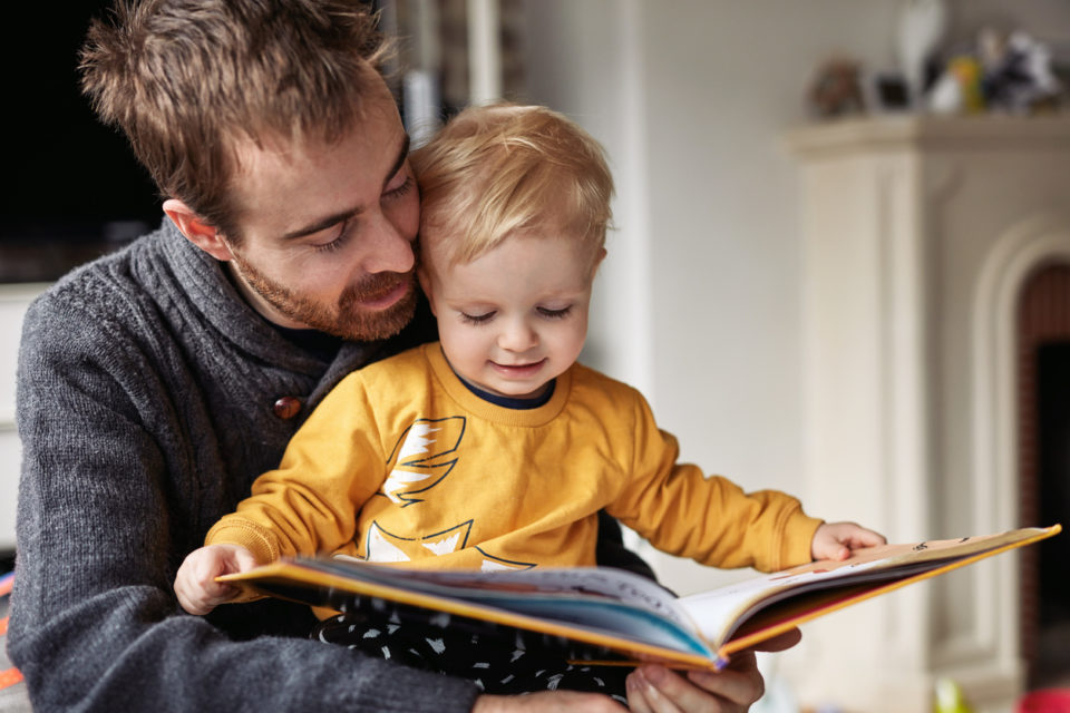 Boy reading a book while sitting with his father at home