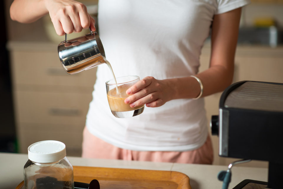 Woman pouring frothed milk into espresso while making a latte