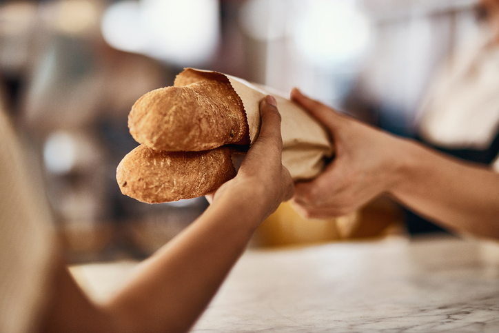 Cropped shot of a woman buying freshly made baguettes at a bakery