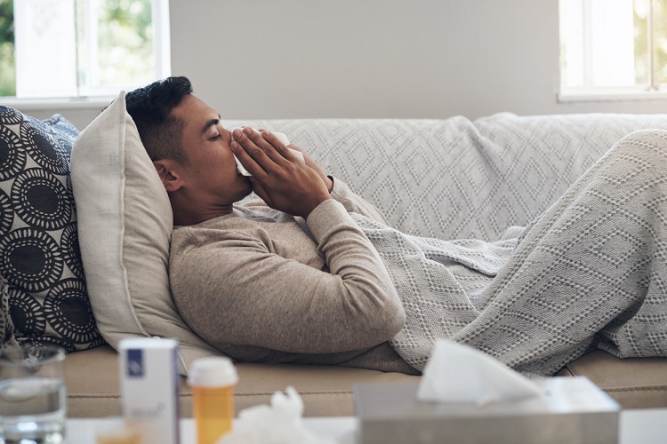 Shot of a young man blowing his nose while feeling sick at home